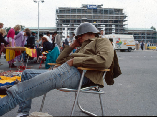 [1990] Scene fra torget ved Brandenburger Tor. Selger av militæreffekter sitter og sover i campingstol, med hjelm trukket ned foran øynene.